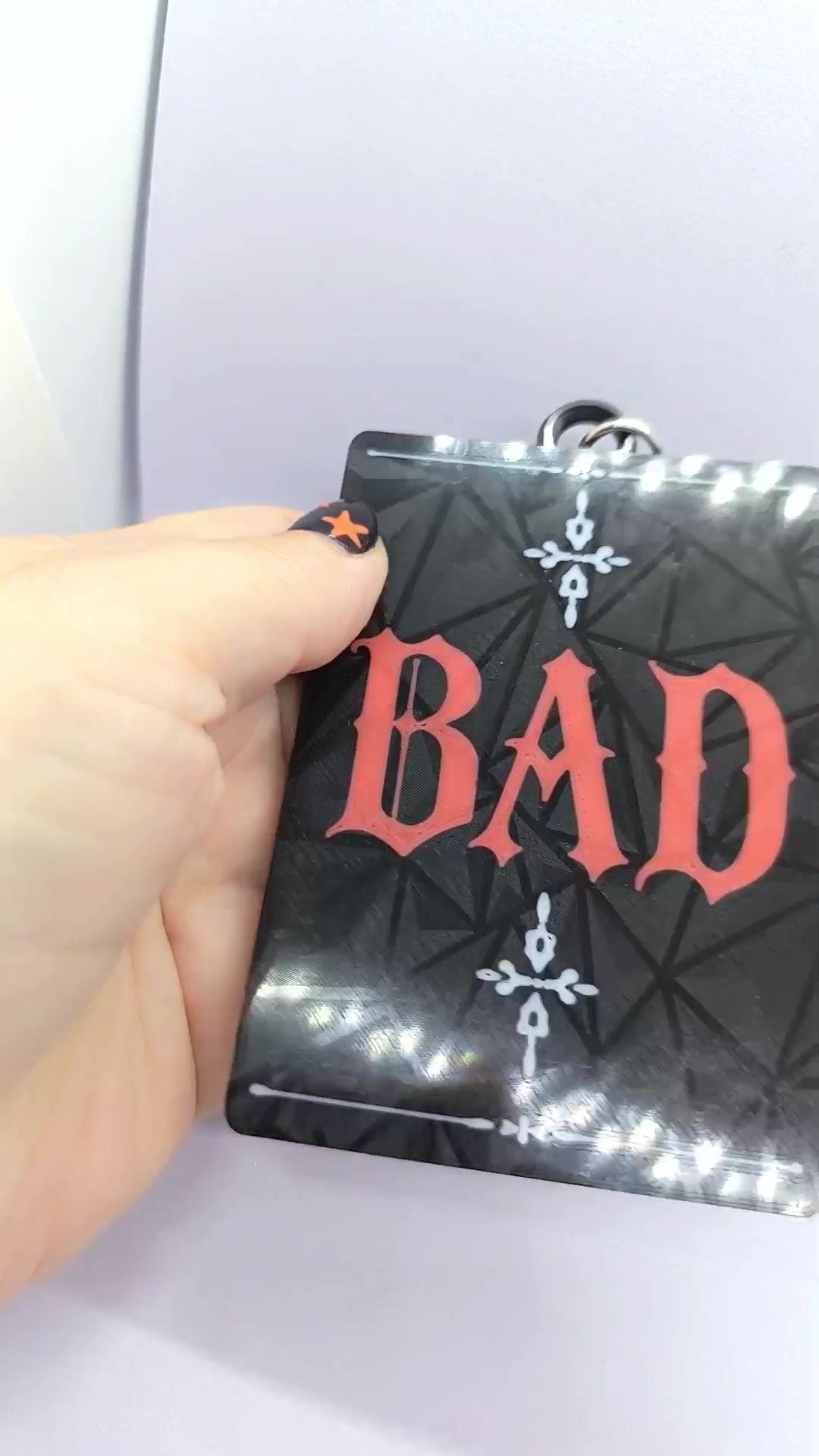 Reverso del holder ATEEZ BAD negro con letras BAD rojas y detalles decorativos blancos.