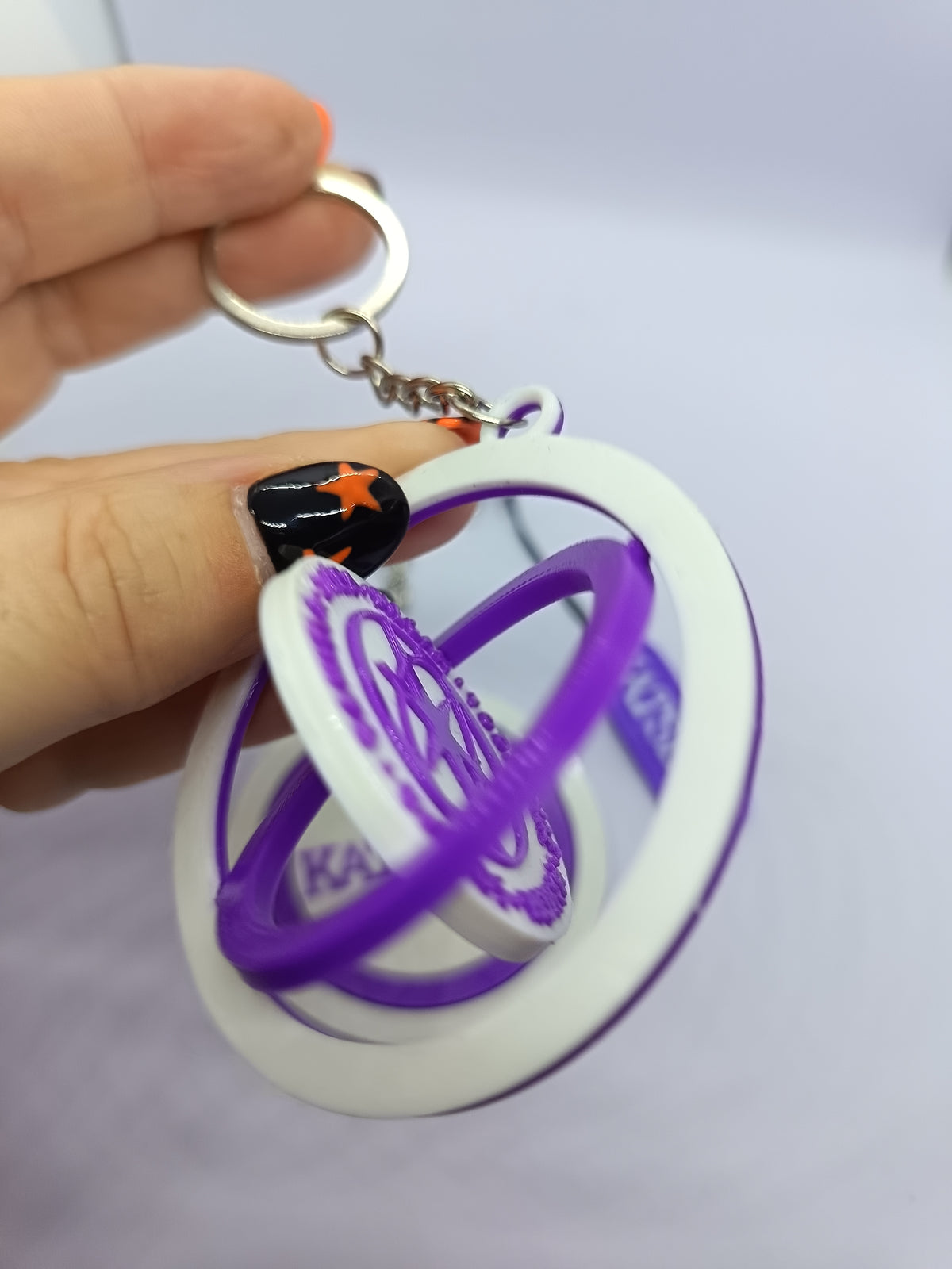 Llavero KATSEYE con logo giratorio morado, fotografía 1 del producto.