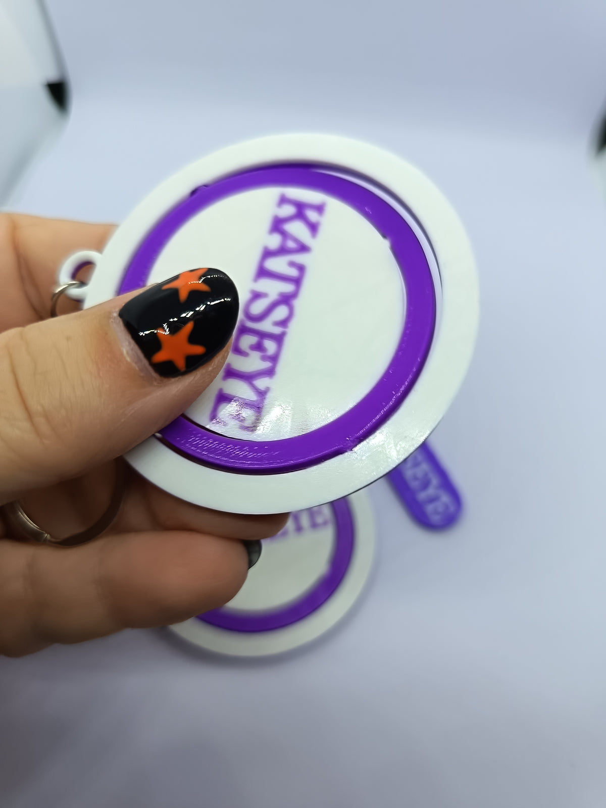 Llavero KATSEYE con logo giratorio morado, fotografía 2 del producto.